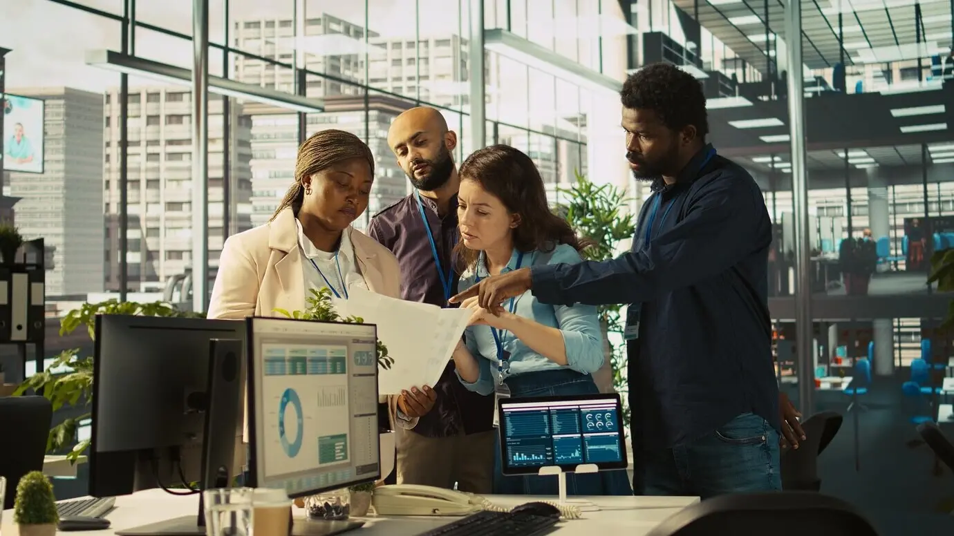 Портрет улыбающихся коллег, просматривающих показатели выручки в бумажных документах.